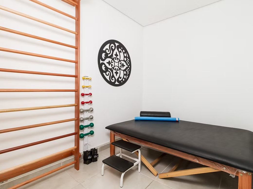 Sala de fisioterapia do Residencial Espaço Saúde com espaldar de madeira, halteres coloridos e mesa de exercícios
