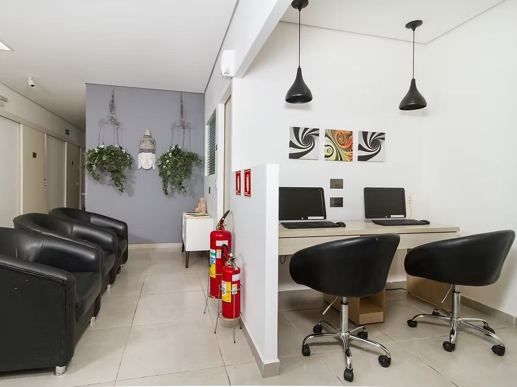 Lan house do Residencial Espaço Saúde com dois computadores e cadeiras, ao lado de poltronas pretas