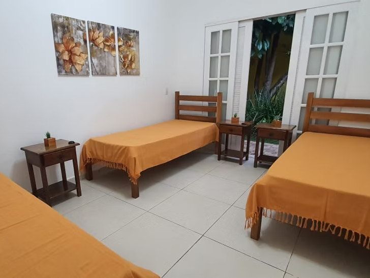 Quarto triplo da Kûara com camas de colcha laranja, criados-mudos de madeira e porta de vidro aberta para o jardim
