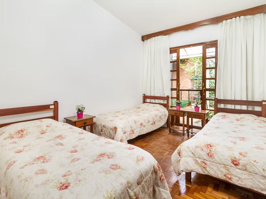 Quarto triplo da Tsuru com três camas de colcha florida, piso de taco e porta de vidro aberta para o jardim