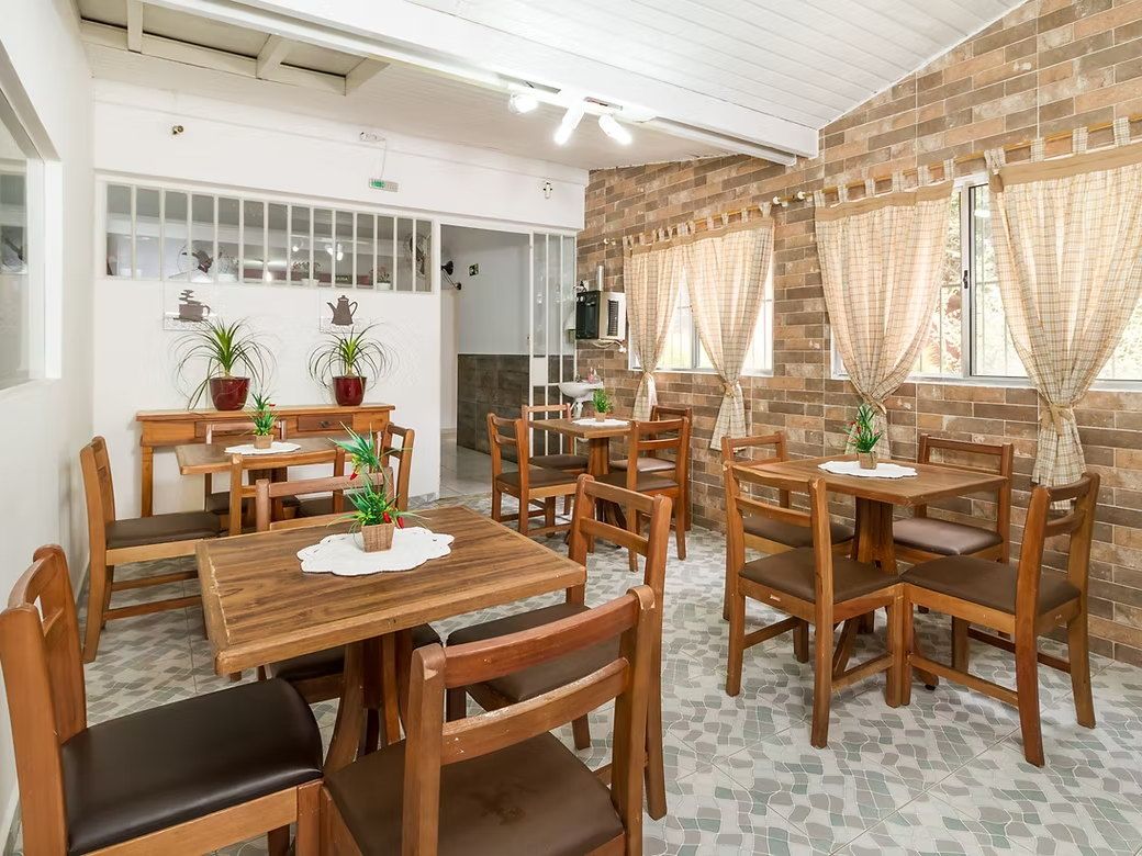 Refeitório da Tsuru com mesas de madeira e toalhinhas de crochê, cortinas xadrez, plantas e parede de tijolos