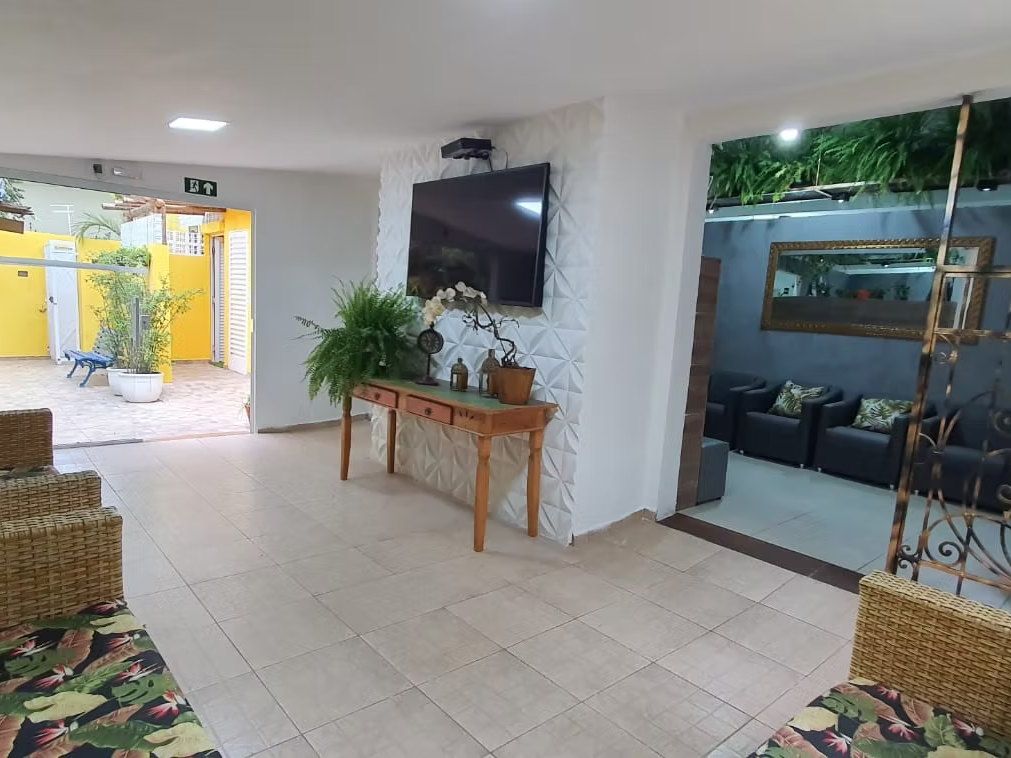 Sala da Kûara com sofás de vime, TV, aparador com plantas e portas abertas para o pátio de parede amarela