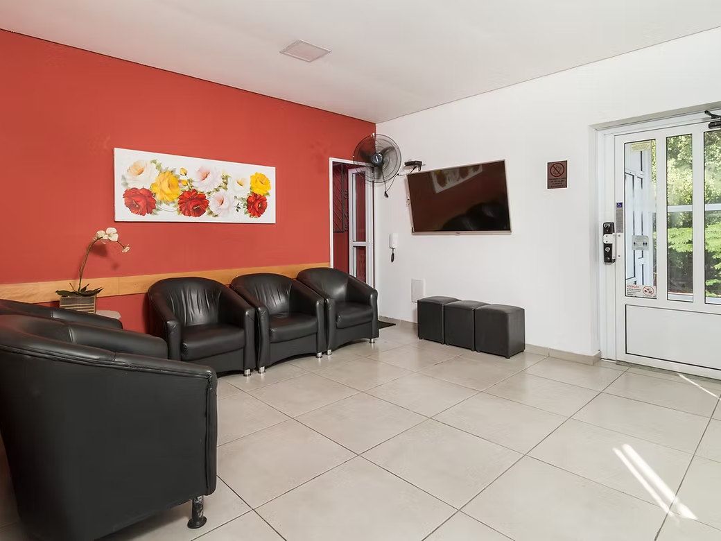 Sala de convivência do Residencial Espaço Saúde com poltronas pretas, parede vermelha com quadro de flores, TV e porta para o jardim