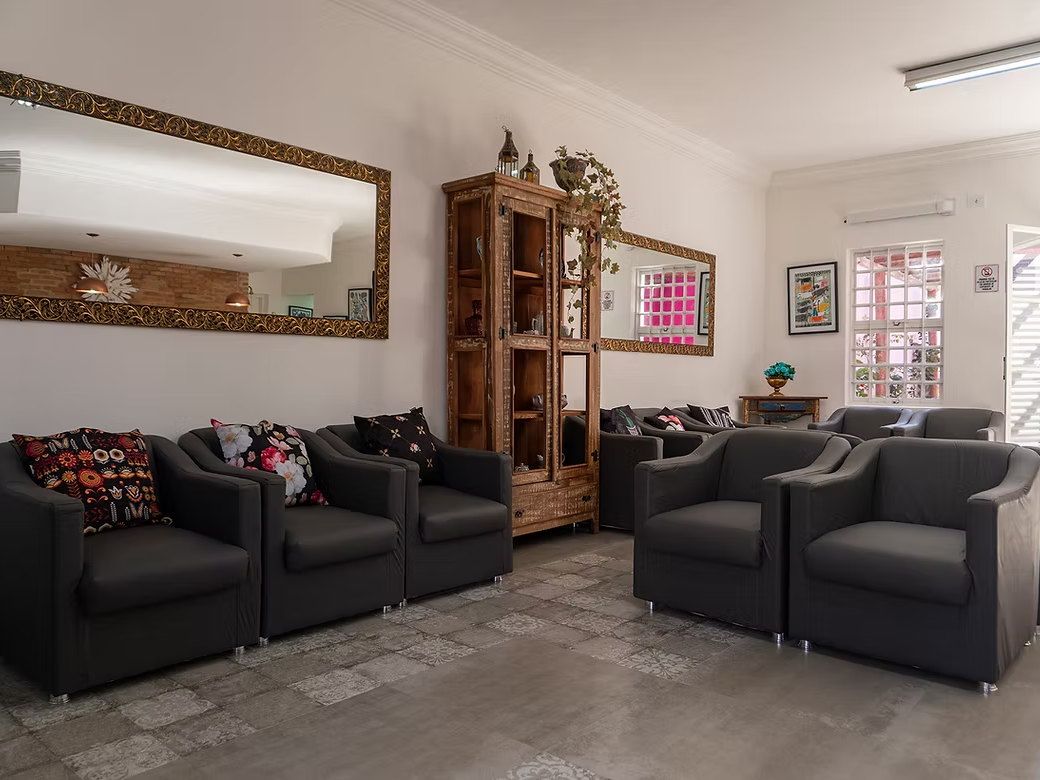 Sala de convivência da La Vie com poltronas cinza e almofadas estampadas, cristaleira de madeira e espelhos de moldura dourada