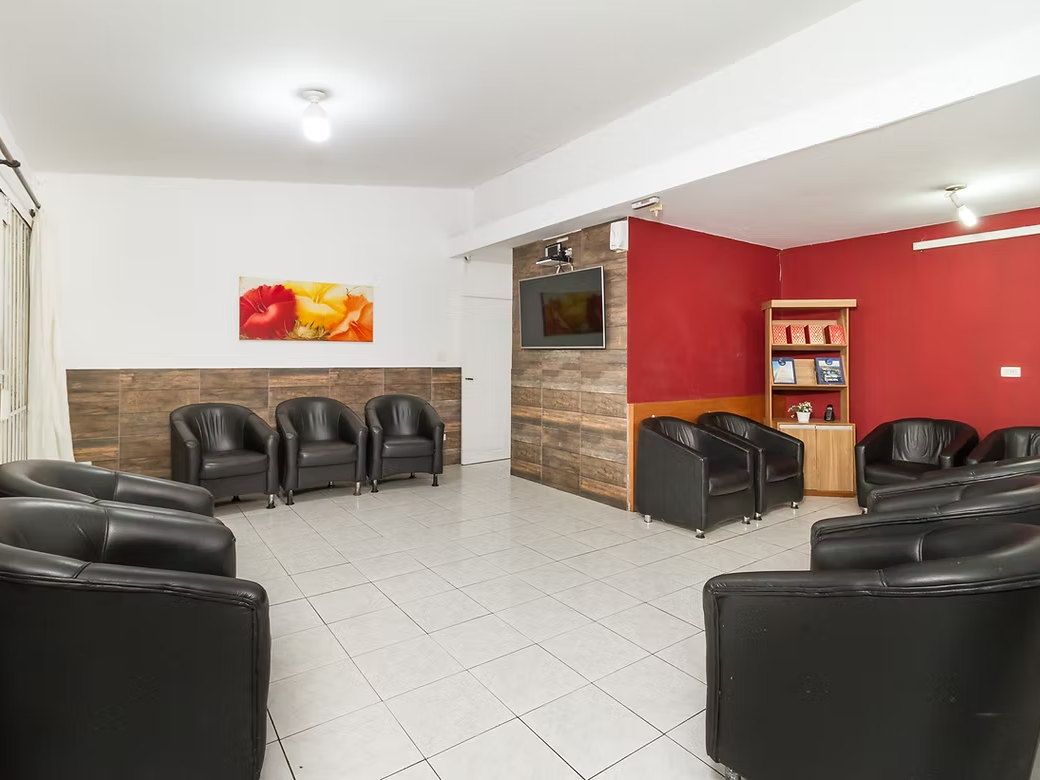 Sala de TV da Tsuru com poltronas pretas, parede vermelha, revestimento de madeira e estante